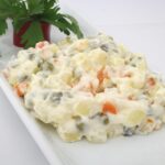 Insalata russa colorata con verdure, maionese e decorazioni festive su un piatto elegante.