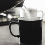 Donna sorseggia acqua calda al mattino, evidenziando i benefici per colesterolo e glicemia.