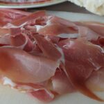 Fetta di prosciutto crudo su un piatto, con ingredienti freschi per abbassare il colesterolo.