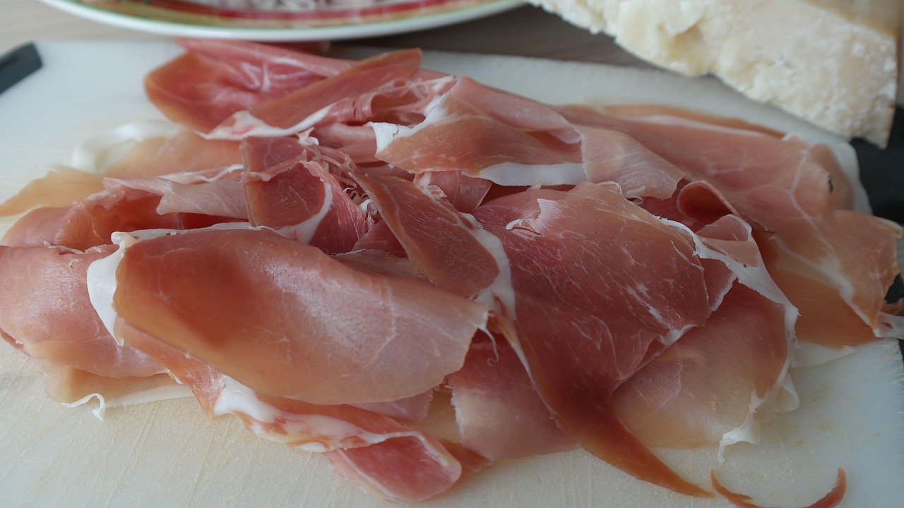 Fetta di prosciutto crudo su un piatto, con ingredienti freschi per abbassare il colesterolo.