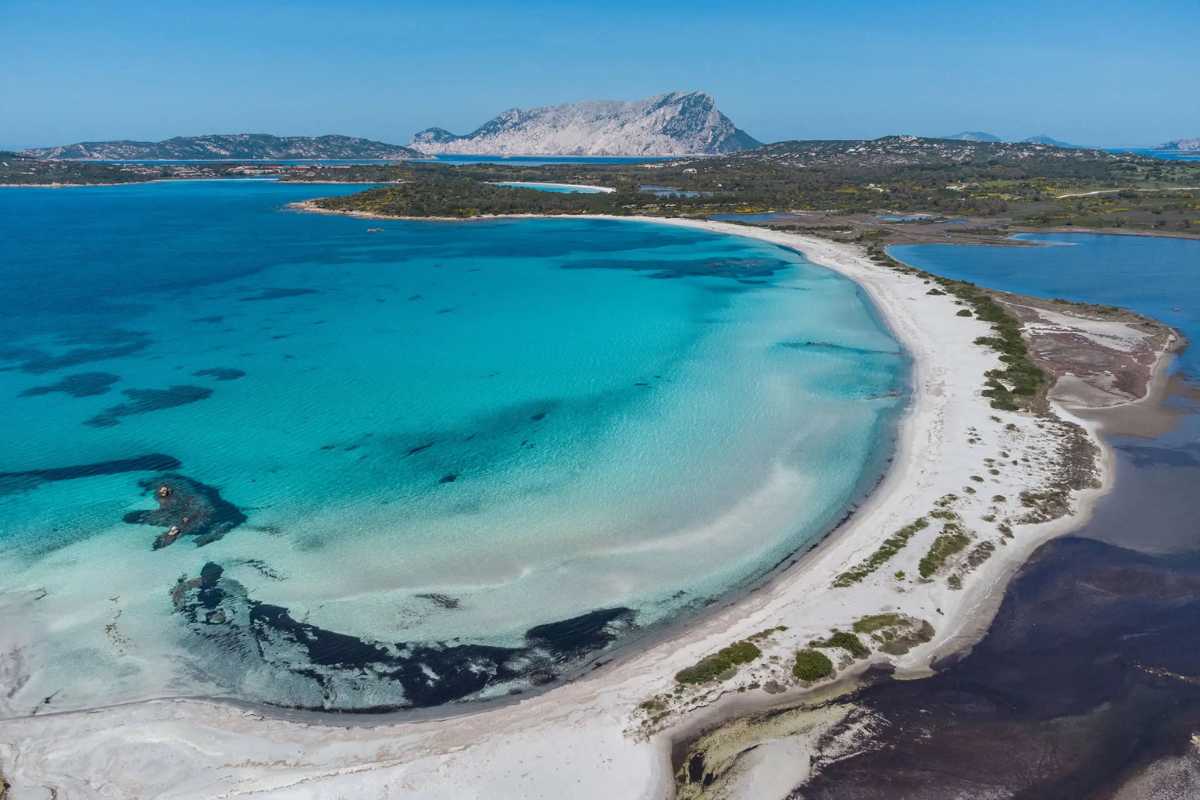 Spiaggia cristallina in Sardegna, con sabbia bianca e acque turchesi, rappresentativa delle bellezze locali.