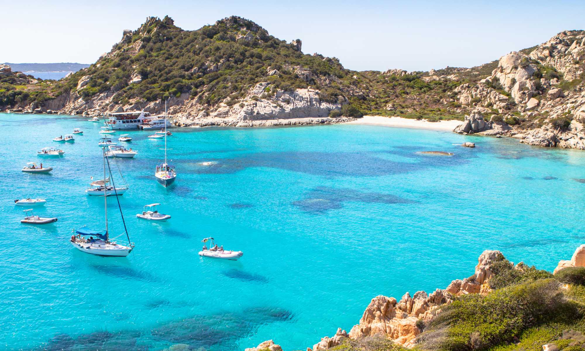 Caletta cristallina in Sardegna, circondata da scogliere e vegetazione mediterranea.